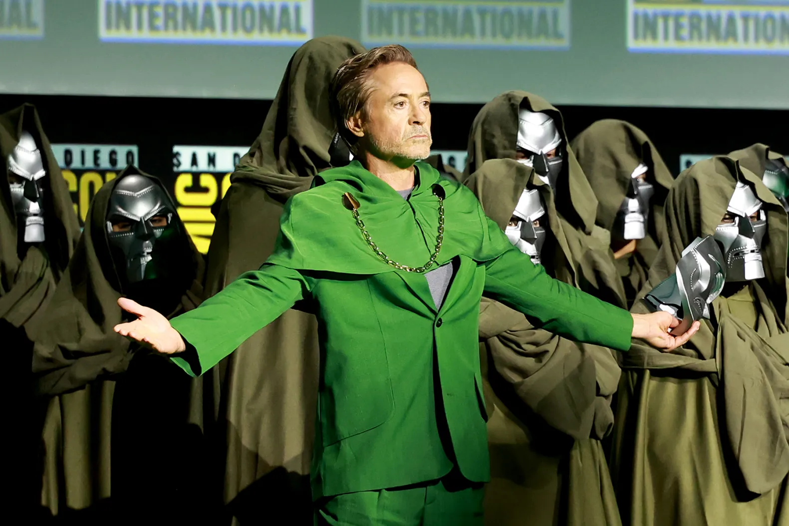 Robert Downey Jr. in a green Doctor Doom robe at San Diego Comic-Con, surrounded by hooded figures in silver Doom masks